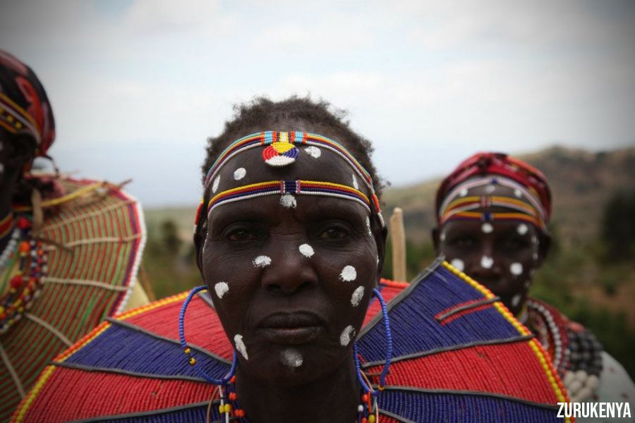 A closeup shot of Kalenjin Tribe member with white fot paints on the face and colorful lines, and a blue and red traditional necklace | Flash mctours and Travel
