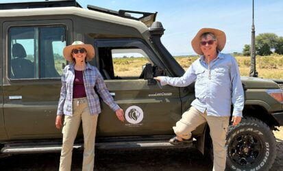 Two travelers posing beside a safari vehicle in the bush