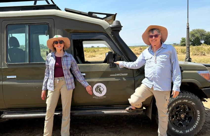 Two travelers posing beside a safari vehicle in the bush