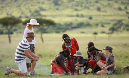 Travelers with children sitting with Maasai community members on the grass