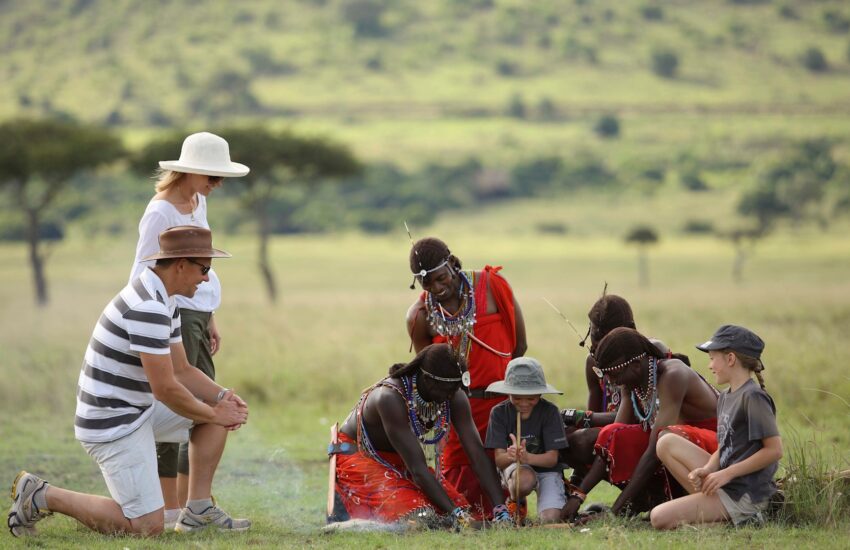 Travelers with children sitting with Maasai community members on the grass
