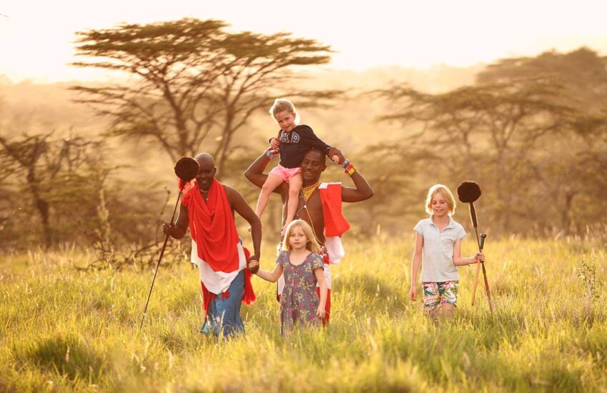 Family with children walking through the savanna with Maasai guides at golden hour